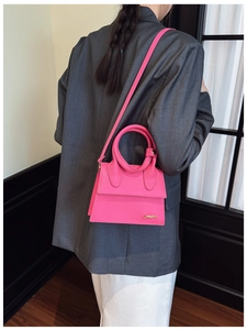 Detail of rose pink leather mini handbag with circular handle and gold logo on grey suit