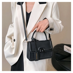 Close-up of black leather crossbody bag with square buckle and fashion tag detail