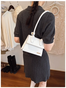 Detail of white leather shoulder bag with gold metal logo shown worn under the arm