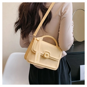 Detail of a creamy yellow crossbody bag with top handle and decorative fashion tag