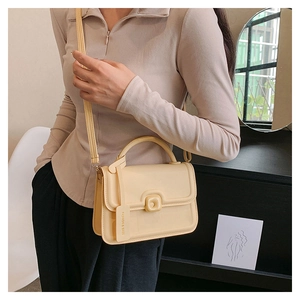 Detail of light yellow square handbag showing flap closure and detachable shoulder strap