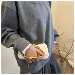 Détail de pochette en cuir blanc avec grande poignée ronde dorée et bandoulière