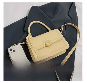 Detail view of a cream square handbag with top handle and phone for size comparison