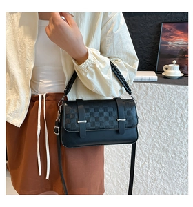 Close-up of black woven checkerboard handbag with metallic buckle and leather texture