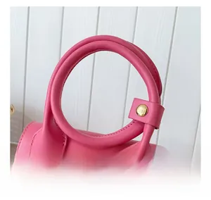 Détail du sac en cuir rose montrant la poignée ronde avec boucles en métal doré