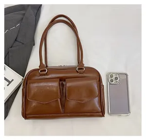 Braune Retro-Tasche mit zwei Vordertaschen neben einem Smartphone zum Größenvergleich