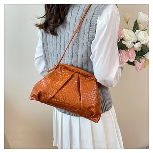 Detail of a brown woven shell bag styled as a crossbody on a model in a minimal setting