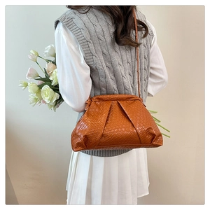Caramel woven texture dumpling bag styled on a model with grey knit vest and white skirt