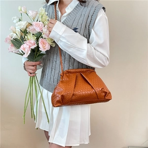 Brown woven crossbody shell bag with gathered closure worn by a model in casual style