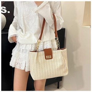 Detail of straw tote bag featuring brown leather straps and gold chain hardware