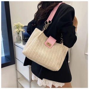 Detail of woven straw tote bag with pink leather strap and gold chain on model