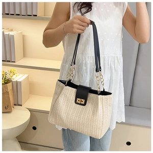 Detail of hand-woven straw tote bag with black leather strap and gold metal clasp