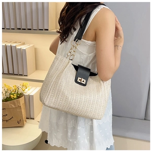 Detail of woven straw tote bag featuring black leather strap and gold metal twist lock