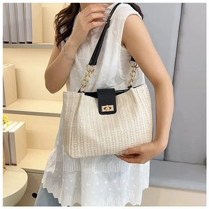 Close-up of woven straw tote bag with black leather strap and golden metal clasp lock