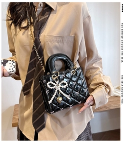 Detail of glossy quilted pattern and pearl bow charm on black patent leather handbag