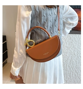Close-up of caramel half-moon saddle bag with golden ring handle on a female model