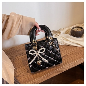 Close-up of black patent leather quilted handbag with pearl bow and golden heart charm
