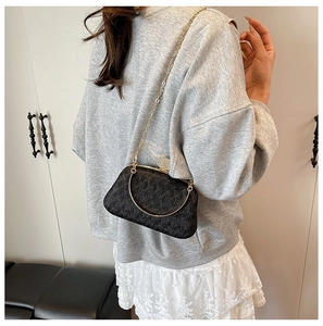 Detail of black textured evening bag with golden ring handle and fine chain shoulder strap
