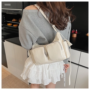 Detail view of cream white patent leather shoulder bag with zipper pockets shown on model