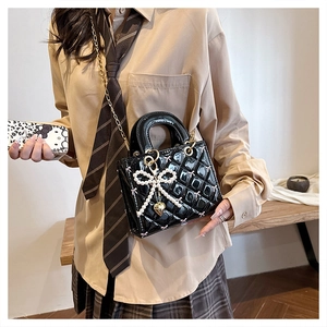 Detail of glossy black quilted patent leather bag with pearl bow and gold heart charm