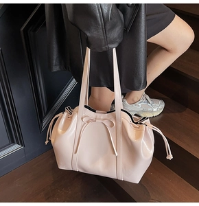 Détail d'un sac cabas en cuir verni rose avec nœud et cordon sur un escalier en bois