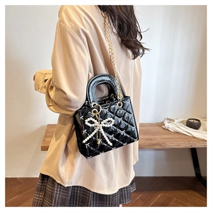 Detail of black patent leather crossbody bag with quilt pattern and pearl bow charm