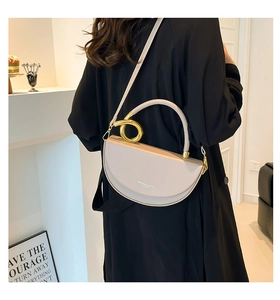 Detail of minimalist beige half-moon bag featuring gold metal ring handle and strap