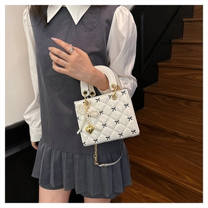 Detail of white quilted patent leather mini bag with bow embroidery and pearl charm