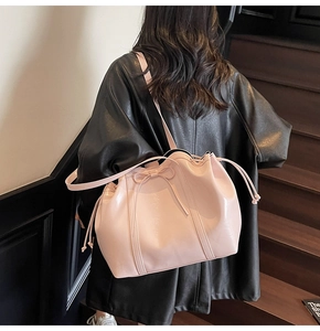 Détail du sac seau en cuir verni rose avec nœud et cordon sur un manteau noir