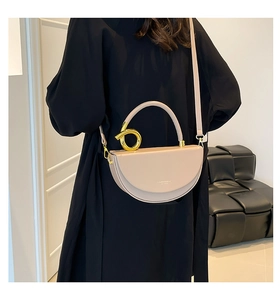 Détail du sac selle en cuir beige avec grande poignée ronde en métal doré et logo doré