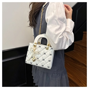 Detail of white quilted patent leather handbag with bow patterns and pearl charm