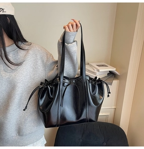 Détail d'un sac d'épaule en cuir verni noir avec nœud coulissant et pompons latéraux