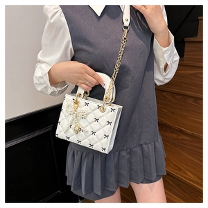 Detail of white quilted patent leather bag with black bows and gold chain strap
