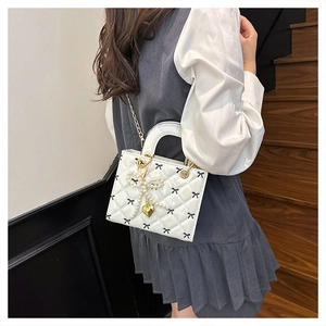 Detailed view of a white quilted patent leather handbag with bow patterns and pearl charms