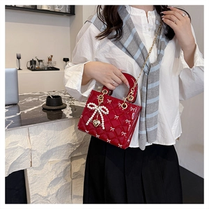 Detail of red quilted patent leather bag with pearl bow and golden heart charm on handle