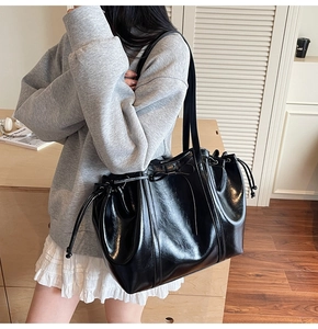 Détail d'un grand sac cabas en cuir noir brillant avec cordon de serrage latéral et nœud