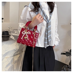 Close-up of red patent leather handbag with bow quilting and pearl butterfly charm