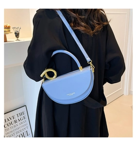 Detail of light blue semi-circular handbag with gold hardware worn by model