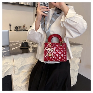 Detail of burgundy patent leather bag featuring quilted bow pattern and pearl charm