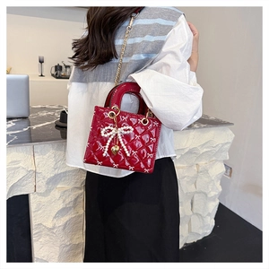 Detail of red quilted patent leather bag with pearl bow charm and gold chain strap