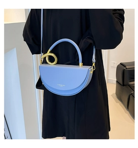 Détail du sac selle bleu ciel avec poignée en spirale dorée et logo blanc imprimé