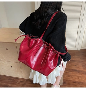 Vue détaillée d'un sac seau en cuir rouge brillant avec cordon et nœud sur un modèle