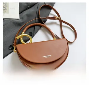 Detail of a brown leather half-moon bag with golden ring and fashion logo on white backdrop