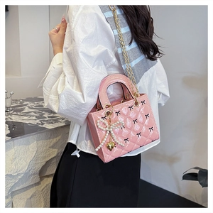 Detail of pink patent leather mini bag with pearl bow charm and golden chain strap