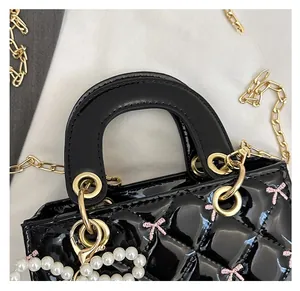 Detail of black patent leather handbag with quilted patterns and pink bow embroidery