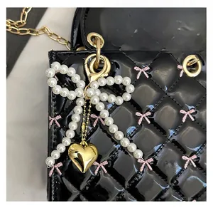 Detail of elegant white pearl bow charm with gold heart pendant on a black handbag