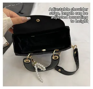 Detail view of the adjustable shoulder strap and pearl charm on a black quilted handbag