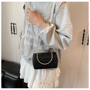 Detail of a black glossy chain bag with gold circular handle and crossbody strap