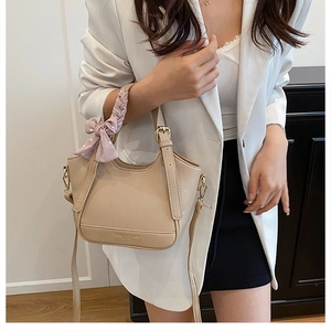 Détail du sac seau à motif litchi avec un nœud rose décoratif en cuir beige