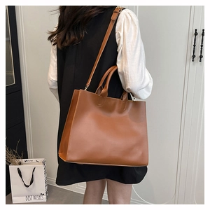 Brown leather tote bag size display on model with adjustable strap and dual handles